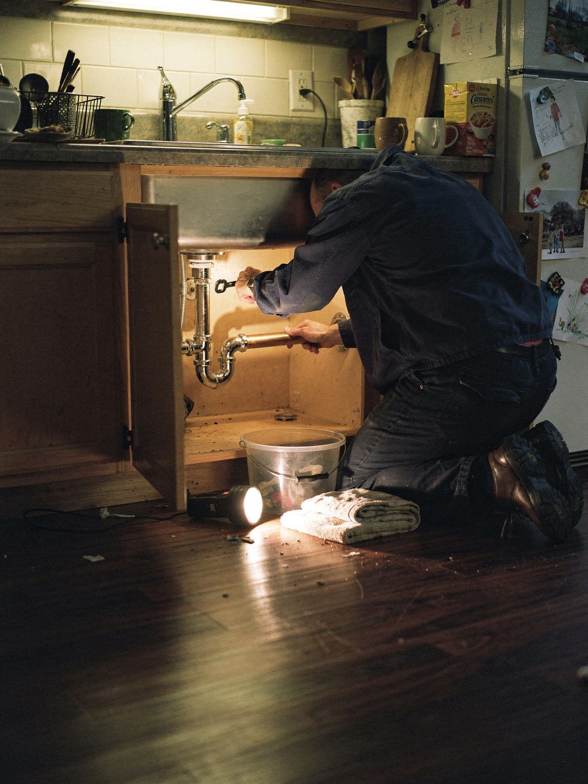 Illustration (AI-generated): A plumber kneeling under a sink with a torch